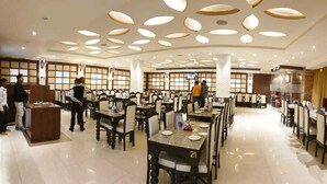 Un restaurante espacioso con varias mesas y sillas, una zona de recepción y un diseño de techo moderno.
