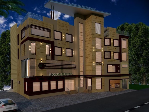 Un edificio moderno con un cartel que dice "MAKHAN RESIDENCY". Tiene varias ventanas y un balcón en el piso superior.