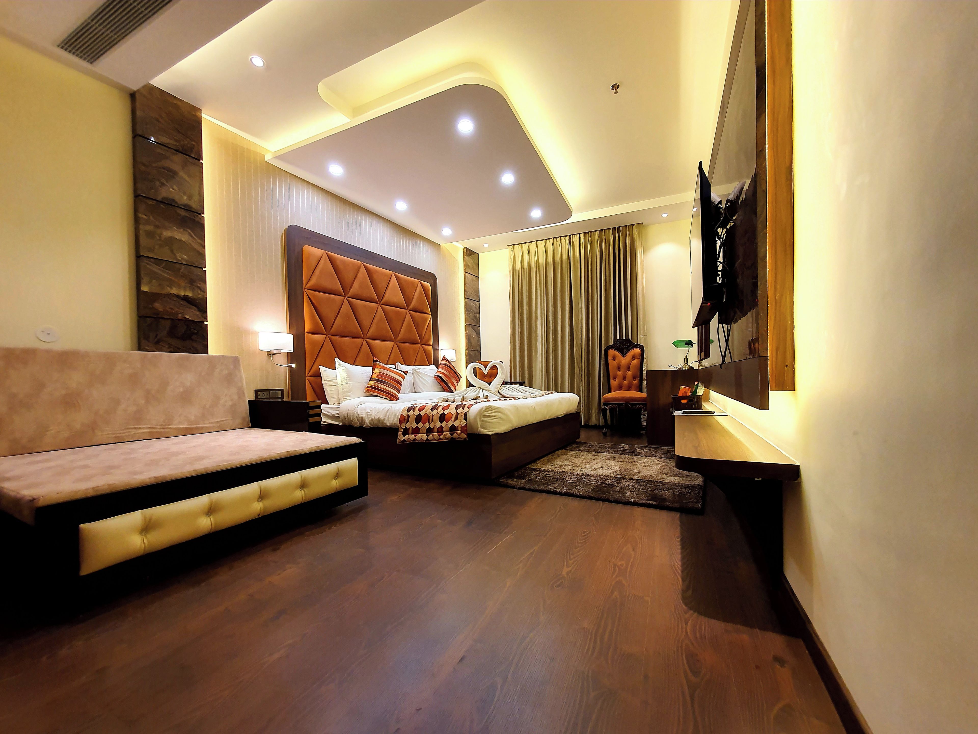 A modern hotel room with a large bed, a sofa, a desk, and a TV.
