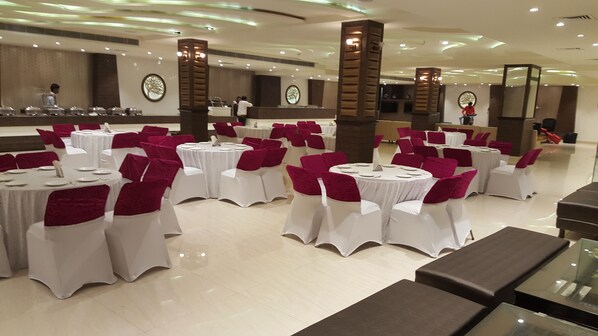 Une salle de banquet avec des tables rondes recouvertes de nappes blanches et des housses de chaise rouges, disposées en rangées.