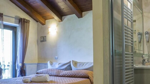 A bedroom with a bed, a bathroom with a shower, and a wooden ceiling. - Il Tintore (Tramonti)