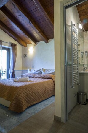 A bedroom with a bed, a bathroom with a shower, and a wooden ceiling. - Il Tintore (Tramonti)