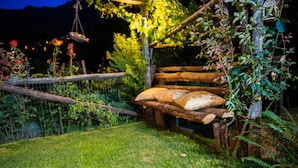 A rustic wooden bench with pillows, surrounded by lush greenery and a wooden fence. - Il Tintore (Tramonti)