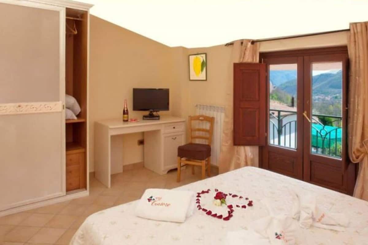 Un dormitorio con cama, escritorio, silla, televisor y vista al exterior.