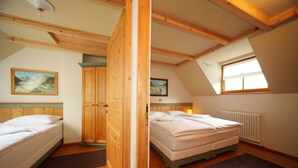 Quarto com duas camas, vigas de madeira, janela com vista e radiador.