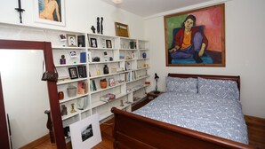 A bedroom with a wooden bed, a bookshelf filled with books and decorative items, a painting on the wall, and a hanging light fixture. - Stay Retro in Soho (London)