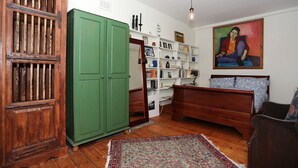 A room with a wooden wardrobe, a green cabinet, a bed with patterned bedding, a bookshelf, and a painting on the wall. - Stay Retro in Soho (London)