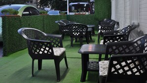 An outdoor seating area with black chairs and tables, surrounded by a green hedge and a white wall. - Admiral Hotel (Kocasinan)