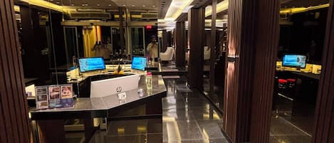 A modern hotel lobby with a central reception desk, mirrored walls, and a polished floor.
