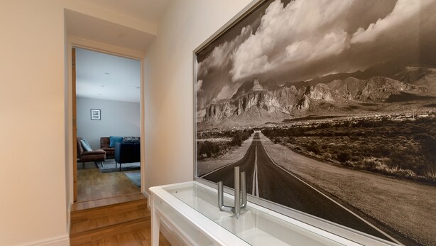 A hallway with a large framed photograph of a mountain road and a modern bathroom with a glass sink. - 3 Beds 2 Baths Penthouse (London)