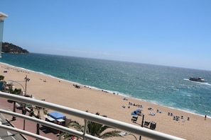 Een strand met helderblauw water, een zandstrand en enkele mensen.