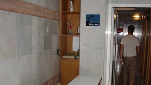 Una zona de recepción con un mostrador de madera, un pequeño estante con objetos religiosos y un cartel que indica la ubicación.