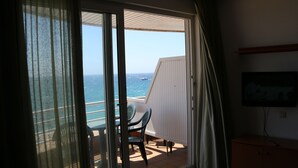 Un balcón con una mesa y sillas, un televisor montado en la pared y vistas al mar.