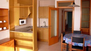 Cocina compacta con armarios de madera, microondas y comedor con mesa y sillas.