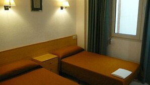 Habitación de hotel con dos camas individuales, una mesita de noche, una lámpara y un ventanal con cortinas.