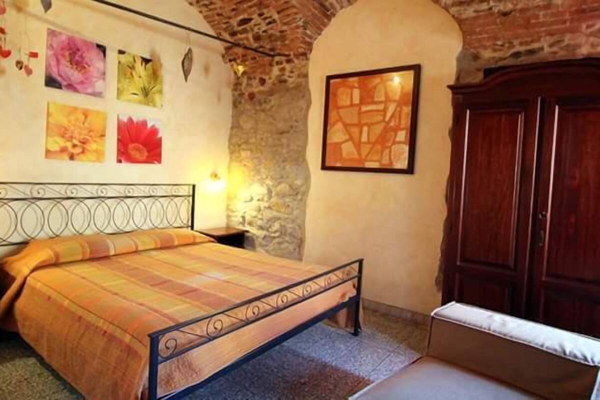 A bedroom with a bed, a wooden wardrobe, and a stone wall.