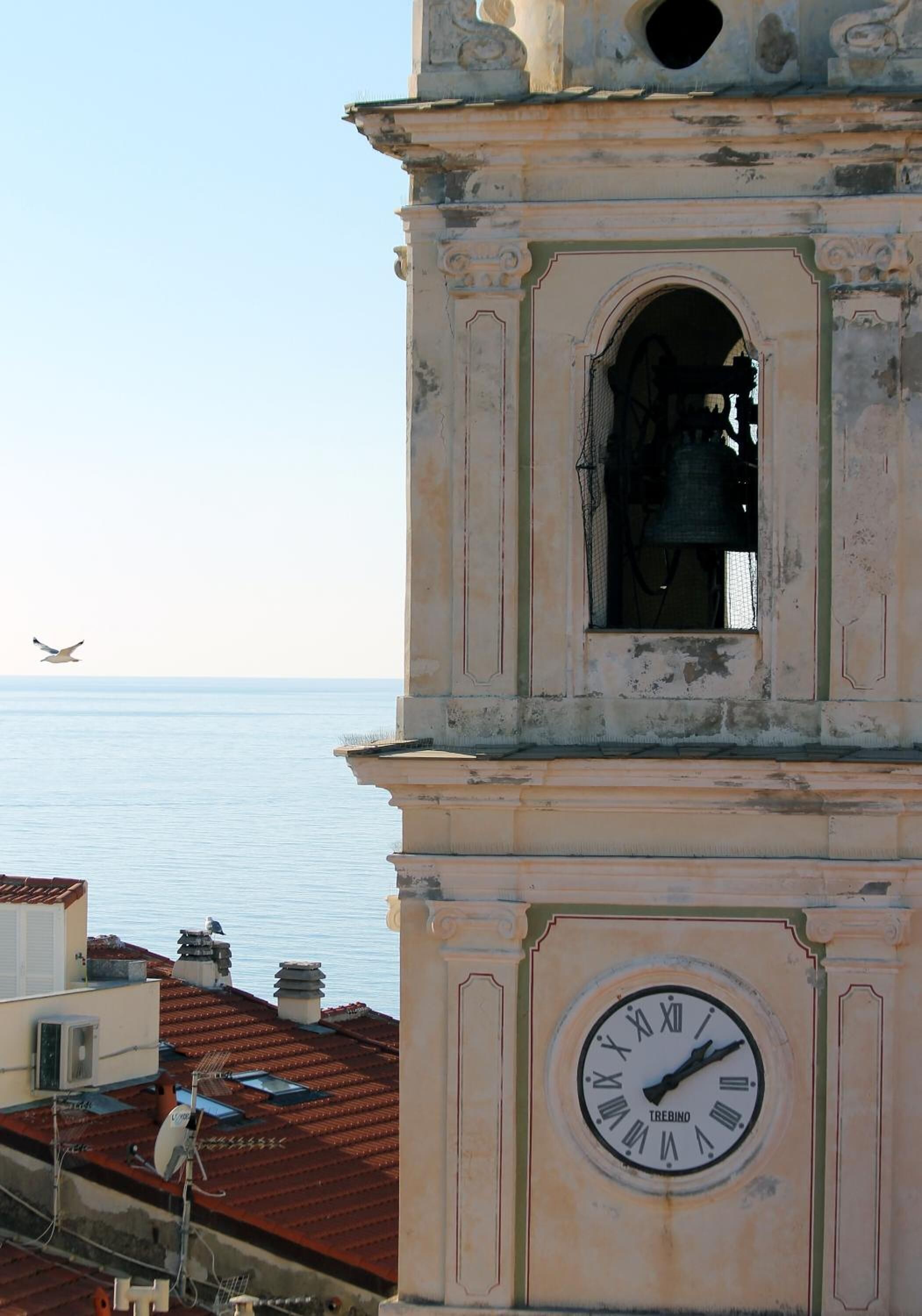 A clock tower with a visible bell and a clear view of the sea in the background.