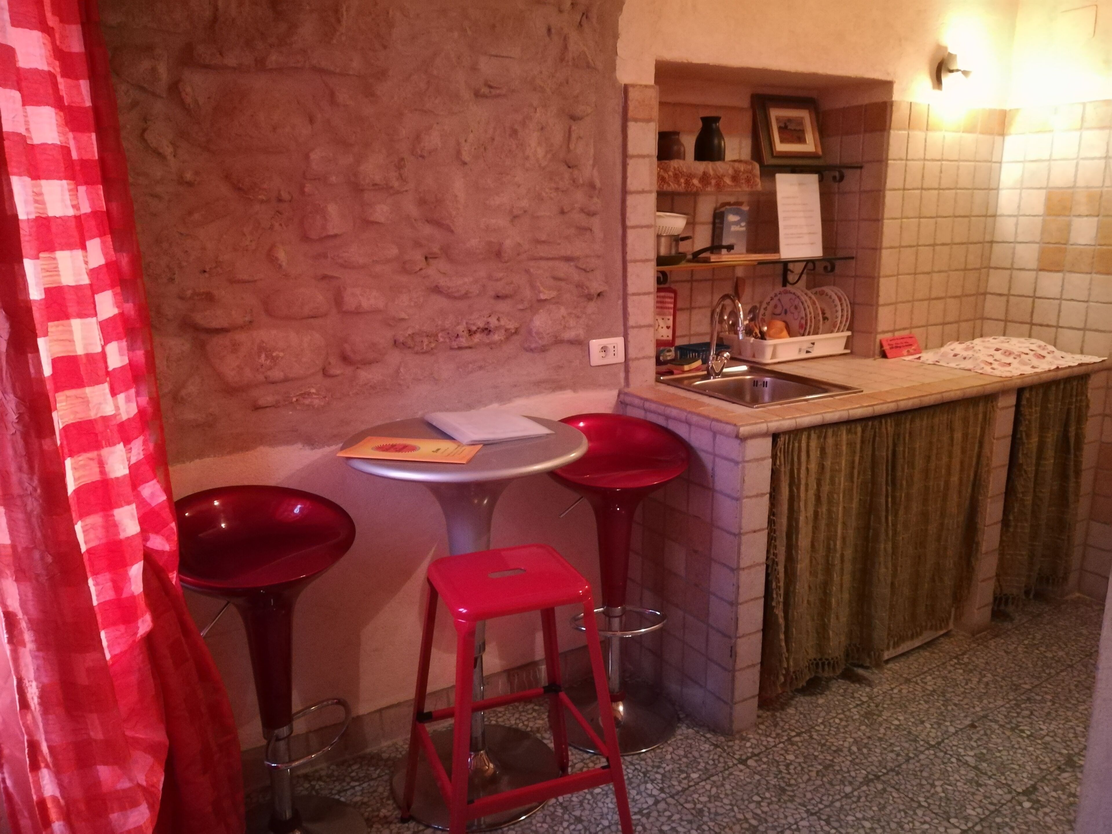 A small kitchen with a stone wall, a sink, and two red stools.