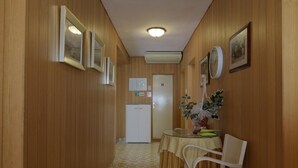 A hallway with wooden paneling, a refrigerator, a table with a chair, and framed pictures on the walls. - Rooms Center of Trogir (Trogir)