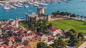 A coastal town with a historic castle, marina with boats, and residential buildings with red-tiled roofs. - Rooms Center of Trogir (Trogir)
