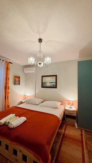 A hotel room with a bed, a nightstand, a lamp, a painting, and an air conditioning unit. - Rooms Center of Trogir (Trogir)