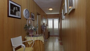 A narrow hallway with wooden walls, a white chair, a table with a yellow tablecloth, and a clock. - Rooms Center of Trogir (Trogir)