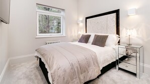 Une chambre avec un grand lit, une table de chevet avec une lampe, une fenêtre donnant sur des arbres et un radiateur.