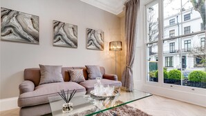 Un salon moderne avec une table basse en verre, un canapé agrémenté de coussins et trois tableaux abstraits accrochés au mur.