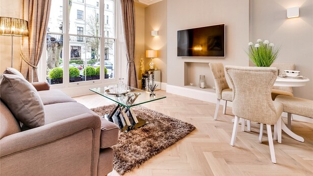 Un salon moderne avec un canapé, une table basse en verre, un coin repas avec des chaises, un téléviseur fixé au mur et une vue sur la ville grâce à de grandes fenêtres.