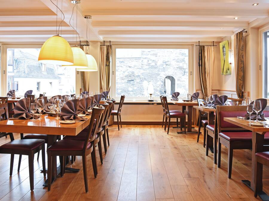 A restaurant with wooden tables and chairs, large windows, and hanging pendant lights.