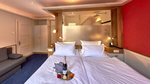 Hotellihuone, jossa on kaksi sänkyä, sohva, minibaari ja punaisella värillä korostettu seinä.