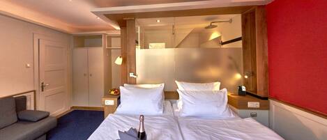 Habitación de hotel con dos camas, un sofá, un minibar y una pared decorada en rojo.