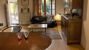 A living room with a sofa, a dining table with two glasses, and a kitchen area with cabinets and a refrigerator. - Vintage houseboat rider ... (Saint-Rémy-de-Provence)
