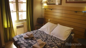 A hotel room with a bed, a chair, a window with curtains, a wall-mounted lamp, and a framed picture. - Vintage houseboat rider ... (Saint-Rémy-de-Provence)