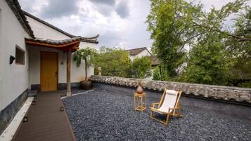A traditional-style building with a tiled roof, a wooden door, and a small garden area with a gravel path, a chair, and a table.