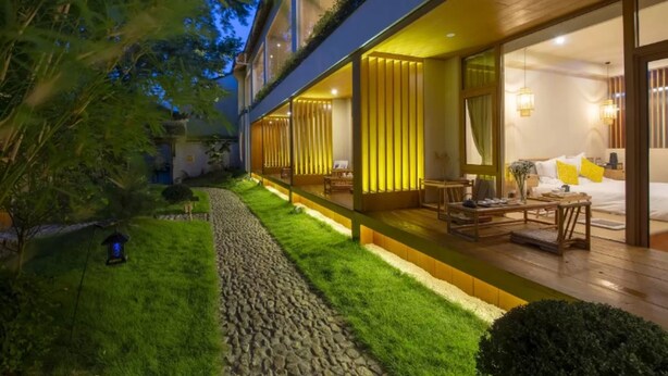 Un bâtiment moderne doté d’un jardin bien entretenu, d’un chemin en pierre et d’un intérieur accueillant comprenant un lit et un coin salon.