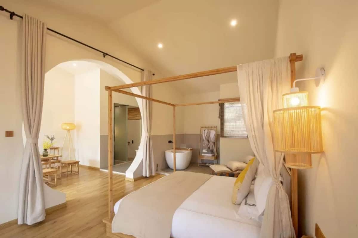 Ein Schlafzimmer mit einem Himmelbett, einem Sitzbereich mit Tisch und Stühlen sowie einem großen Fenster mit Vorhängen.