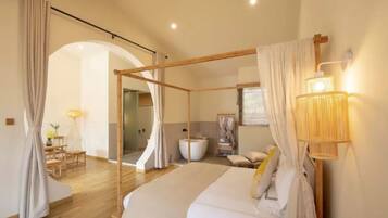 A bedroom with a four-poster bed, a sitting area with a table and chairs, and a large window with curtains.