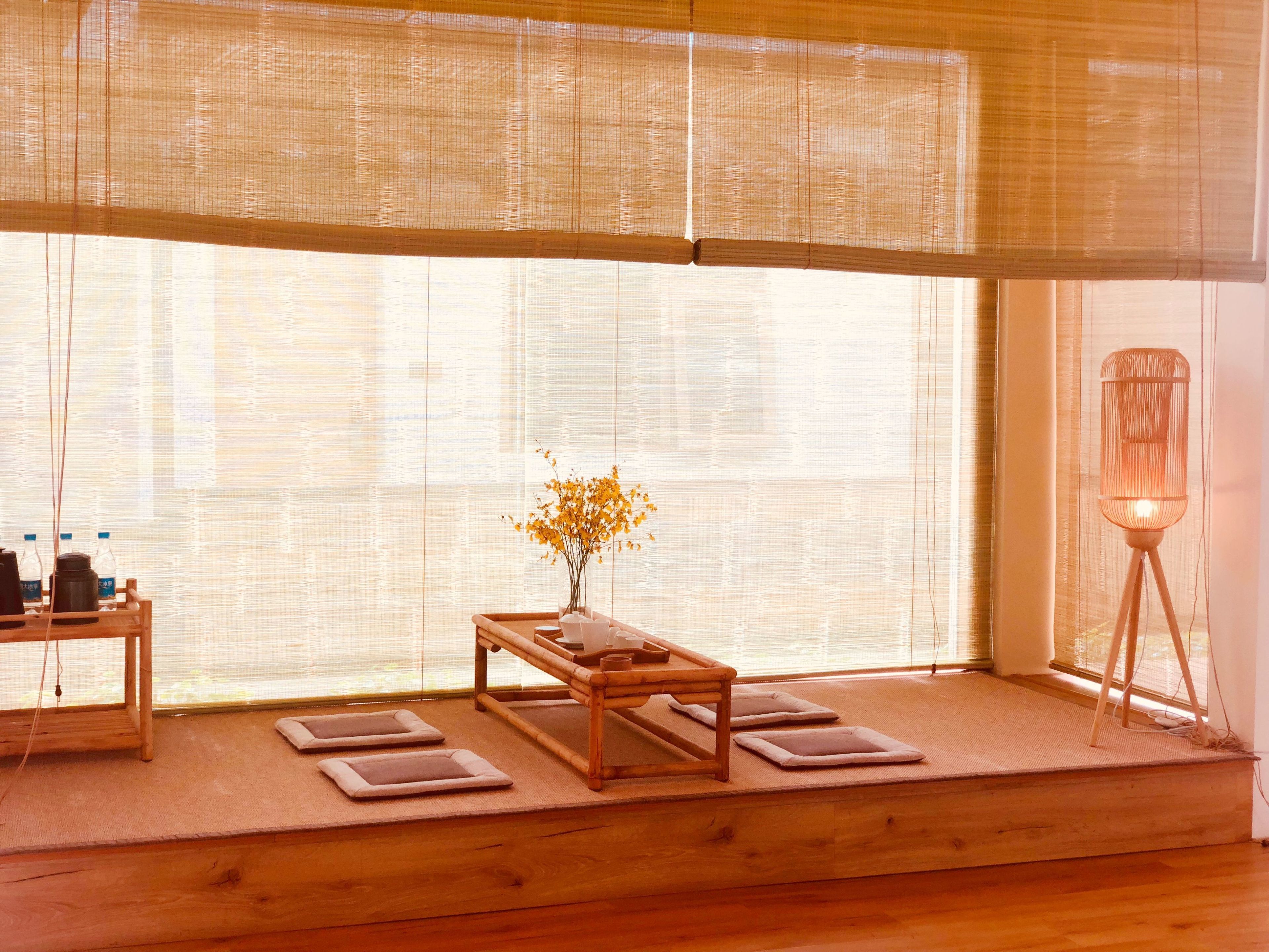 Une pièce de style japonais traditionnel, avec un sol recouvert de tatamis, une basse table en bois entourée de coussins, un vase rempli de fleurs et un lampadaire.