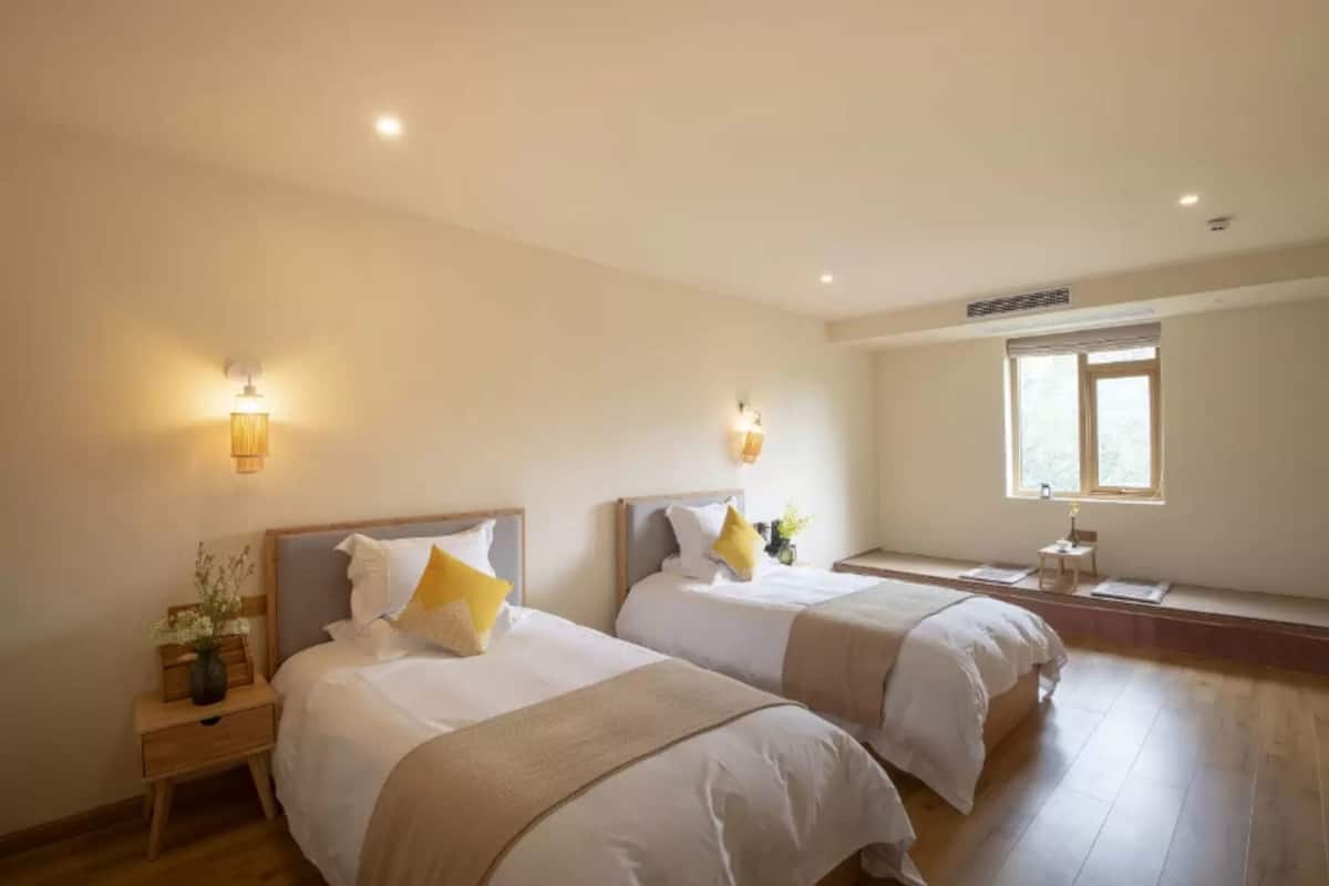Ein Hotelzimmer mit zwei Betten, Nachttischen, Wandlampen, einem Fenster und einem Deckenventil.