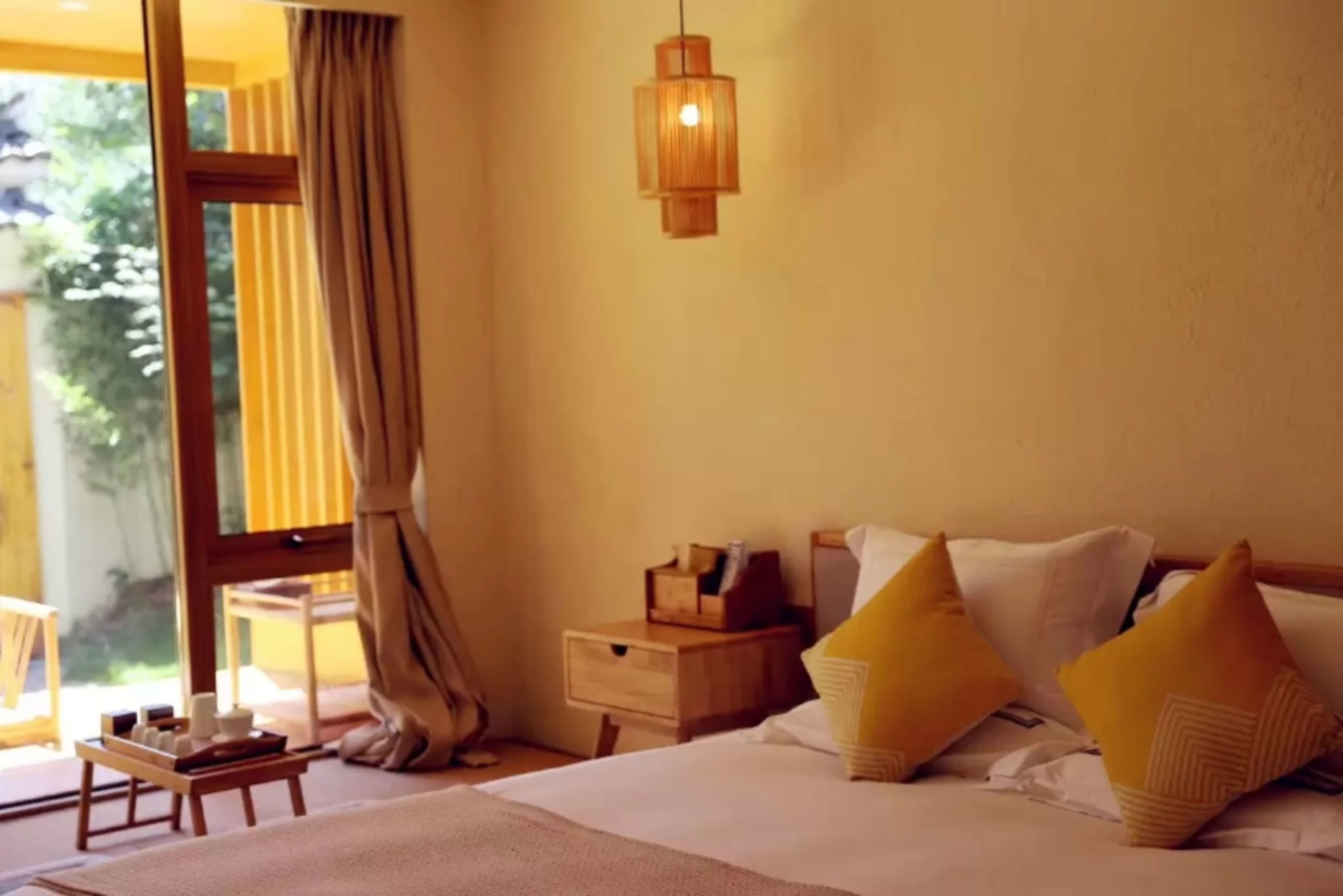 A hotel room with a bed, bedside table, nightstand, and a hanging light fixture.