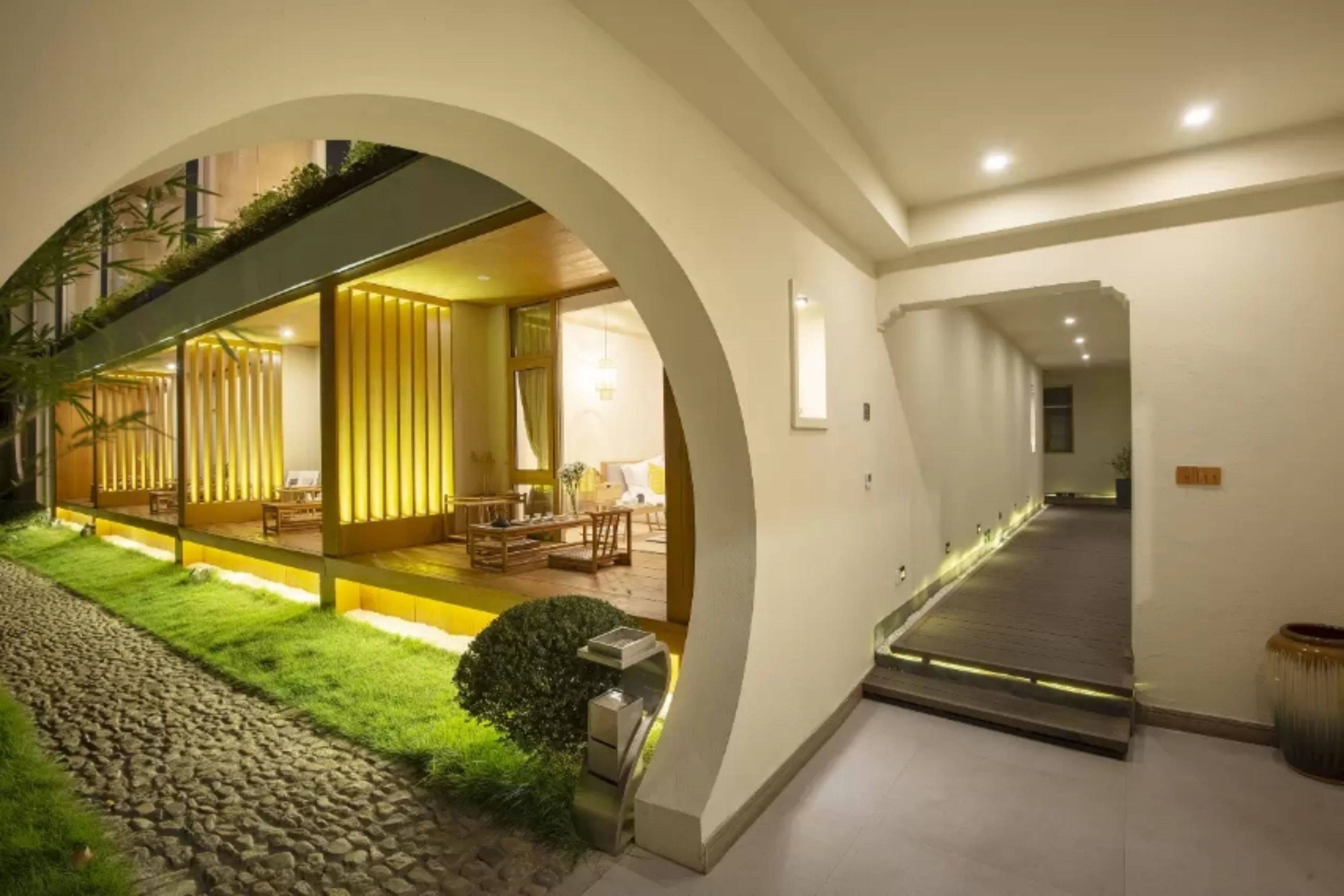 A modern interior with a long hallway, a seating area with yellow walls, and a staircase.