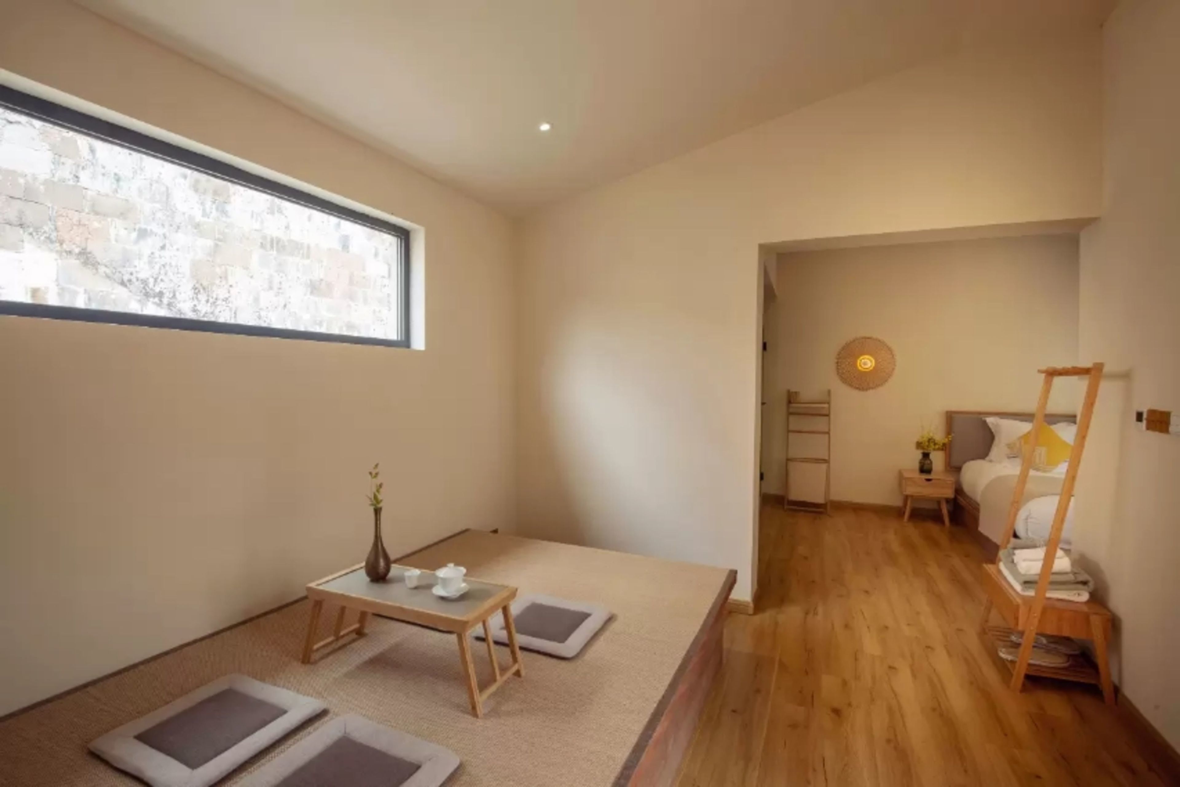 A minimalist room with tatami mats, a low table with tea set, a bed with a wooden ladder, and a small window with a view.