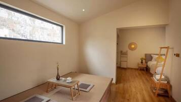 A minimalist room with tatami mats, a low table with tea set, a bed with a wooden ladder, and a small window with a view.
