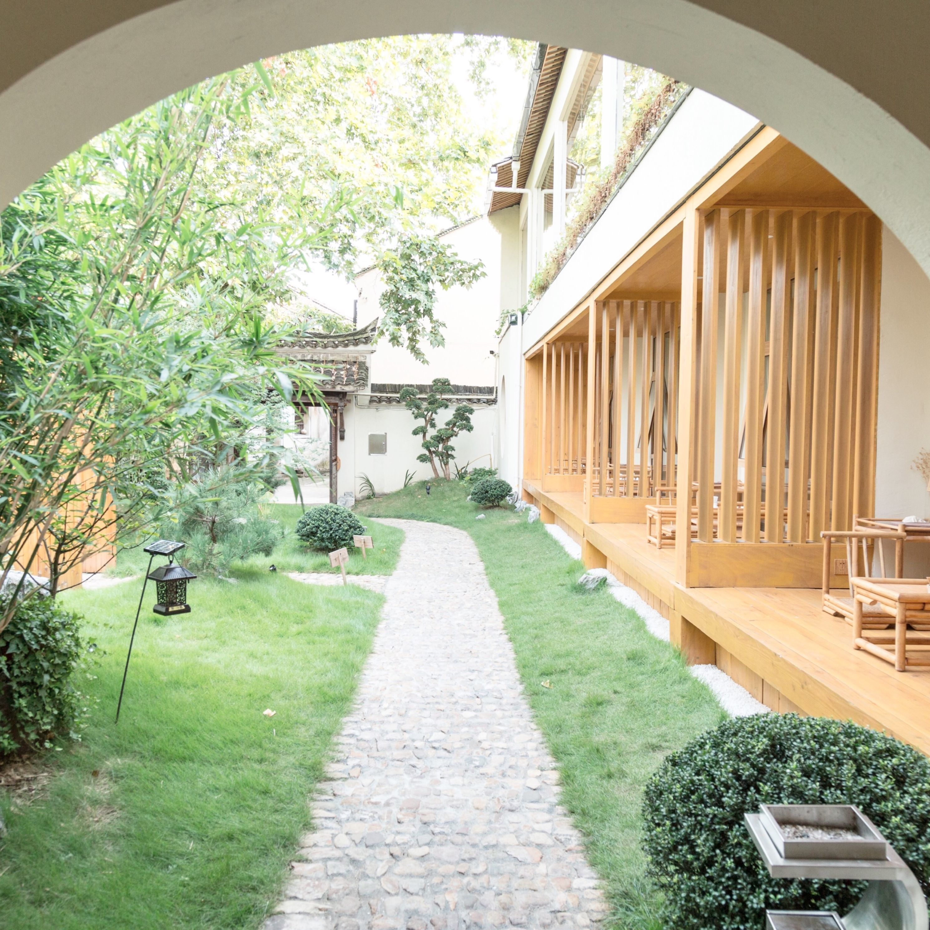 A courtyard with a stone pathway, wooden furniture, and greenery.