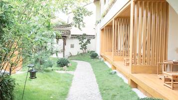 A courtyard with a stone pathway, wooden furniture, and greenery.