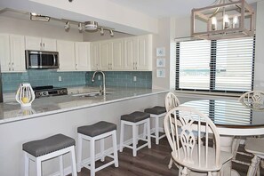 A kitchen with white cabinets, a microwave, a stove, and a bar area with stools and a table.
