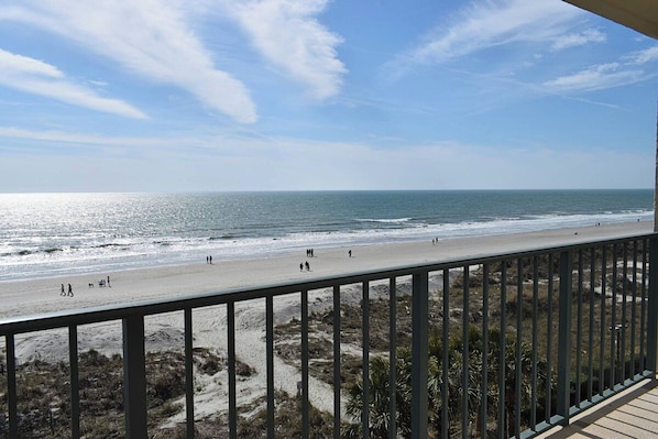 A beach with a clear sky, a sandy shore, and a railing in the foreground.
