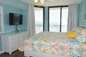 A bedroom with a bed, a television, a dresser, and a balcony with a view.