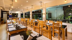 Un restaurante con varias mesas y sillas, ventanas amplias y lámparas colgantes.